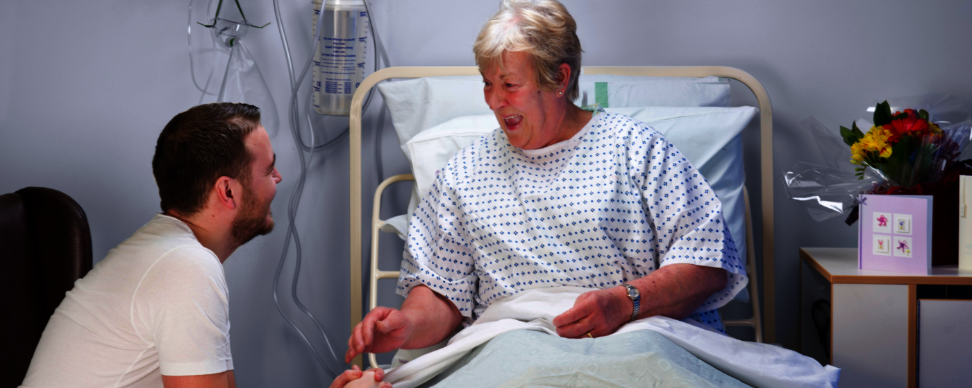 Junger Mann im Gespräch mit älterer Dame am Patientenbett