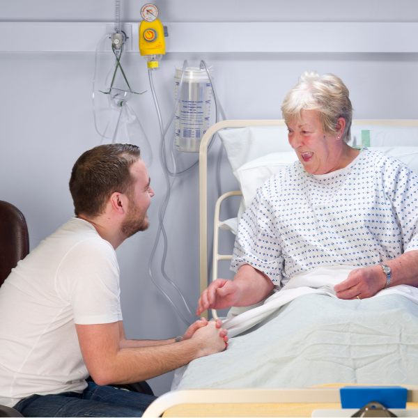 Junger Mann im Gespräch mit älterer Dame am Patientenbett